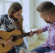 Man teaching woman to play guitar indoors